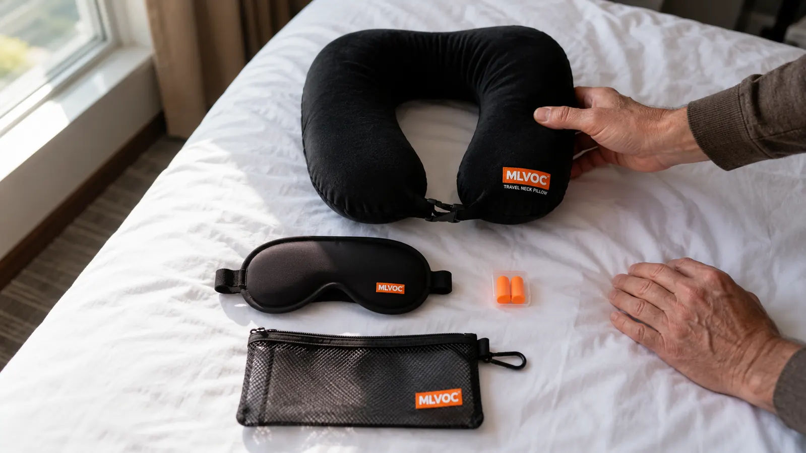 The MLVOC travel kit laid out on a hotel bed: memory foam pillow, 3D eye mask, foam earplugs, and mesh carry bag